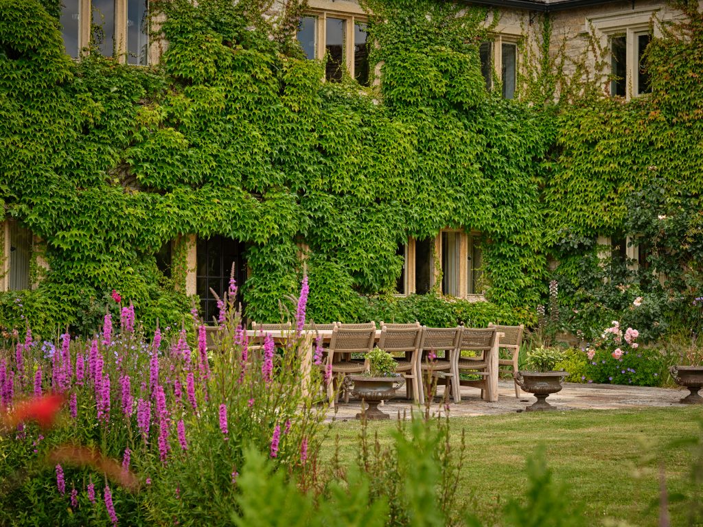 A landscaped Cotswolds garden with stone house backdrop, reflecting the calm elegance and natural setting of a luxury country home.